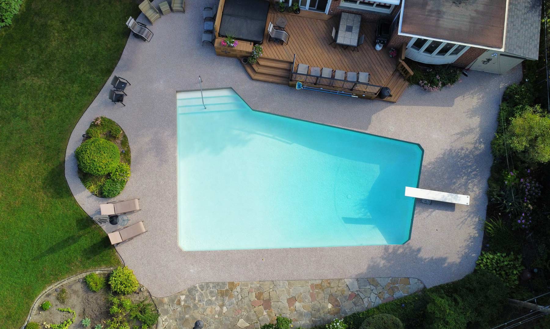 Aerial view of a backyard swimming pool surrounded by grey poured rubber surfacing installed by Rubber Decker