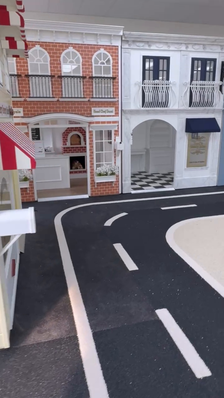 Curved black rubber roadway beside playhouse storefronts at Beyond Play in Barrie